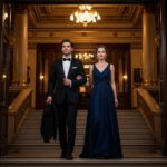 Pár ve večerních šatech vstupuje do velkého filharmonického sálu s osvětlenými schody a zlatými detaily