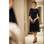 Elegantní žena v černých krajkových šatech s šperky a kabelkou v luxusním interiéru s teplým osvětlením