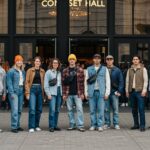 Skupina mladých lidí před vchodem do koncertní haly v neformálním oblečení, s rušným pozadím.