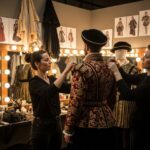 Kostýmní návrhář a maskér spolupracují na jevišti při přípravě renesančního kostýmu.