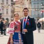 Mladý pár v tradičním československém oděvu na náměstí s vlajkami a oslavami za slunečného dne