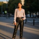 Mladá žena ve městě v kožených kalhotách a světle pastelové blůze při zlaté hodině