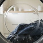 Přední pračka v chodu s modrými džínami a kapkami vody na skle bubnu v moderní prádelně
