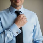 Muž v modré košili a černé kravatě na rozmazaném neutrálním pozadí, detail horní části těla